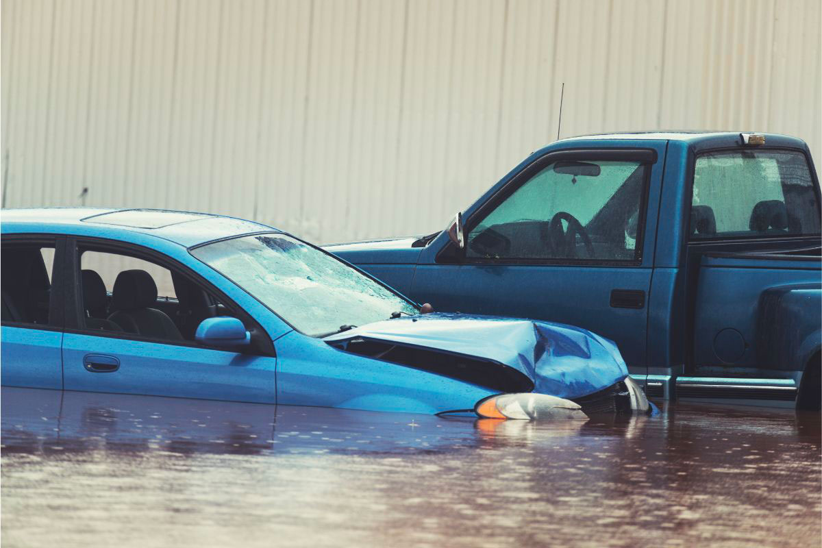 A crashed car and a 4x4 partially submerged in a flood, with water submerging the vehicles and rendering them inaccessible.